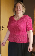 Woman wearing a pink knitted top and black skirt indoors.