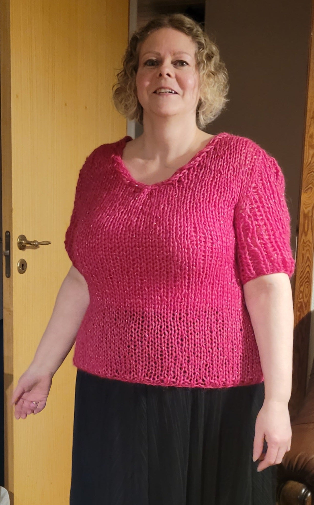 Woman wearing a pink knitted top and black skirt indoors.
