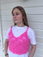 Person wearing a pink knitted tank top over a white shirt against a white wall.