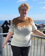 Woman standing on a metal staircase with a clear blue sky and building in the background. She's wearing a white and brown sweater.
