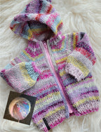 Colorful knitted baby jacket with a matching yarn ball on a fluffy white surface