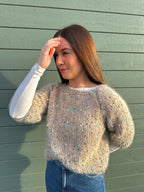 Woman wearing a sequined sweater against a green wooden wall