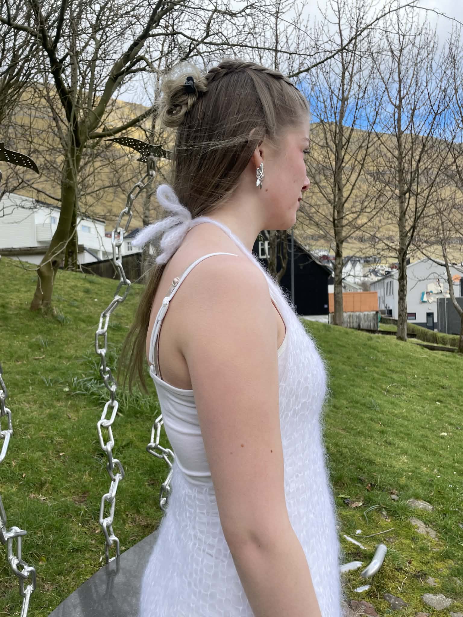 Young woman in a white, knitted dress standing outdoors with trees and grass in the background