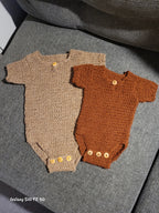 Crocheted brown and beige baby rompers with buttons on a gray sofa