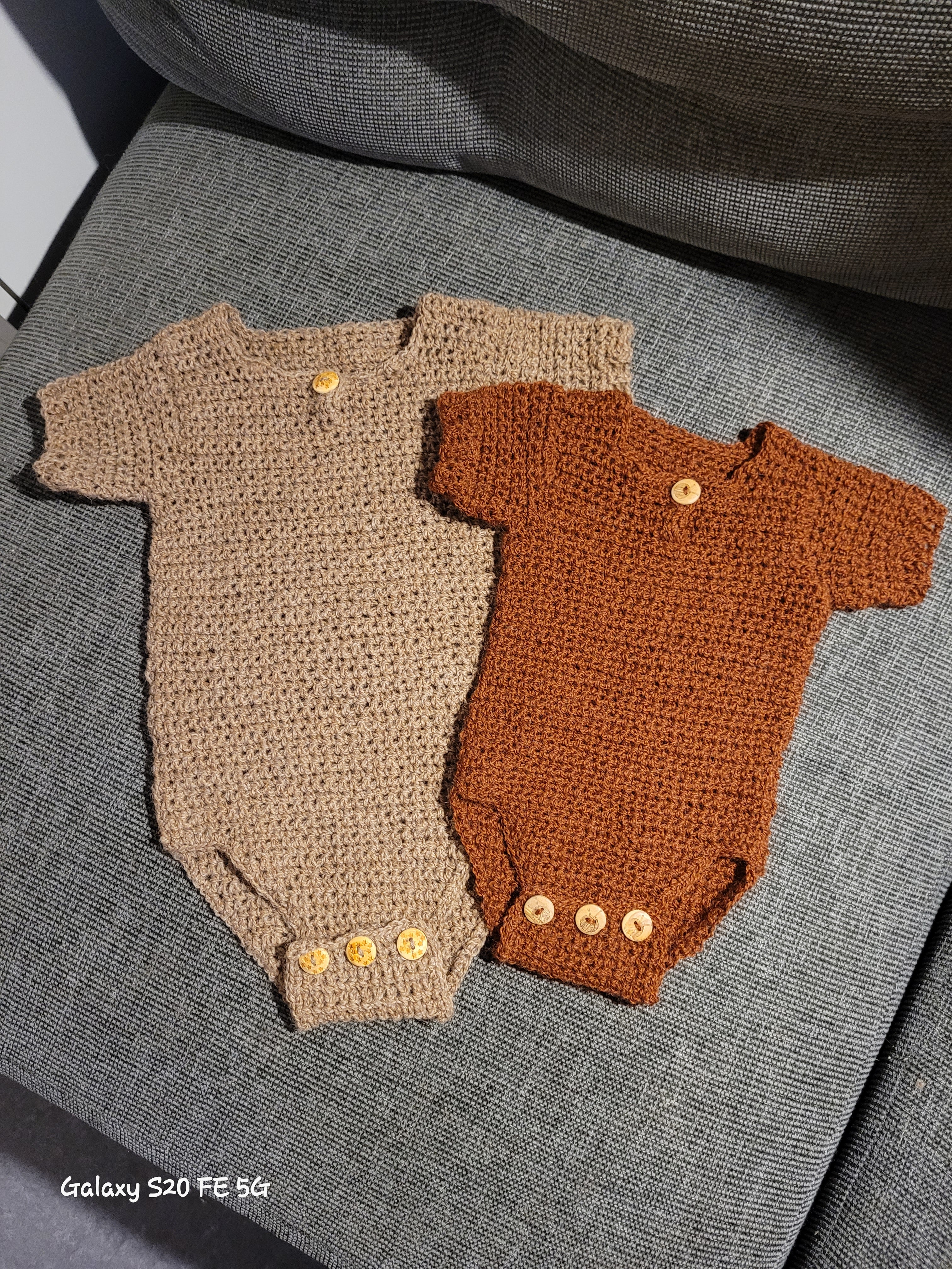 Crocheted brown and beige baby rompers with buttons on a gray sofa
