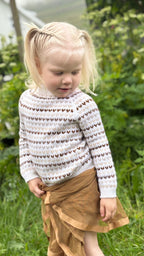 Child wearing a patterned sweater and brown skirt outdoors