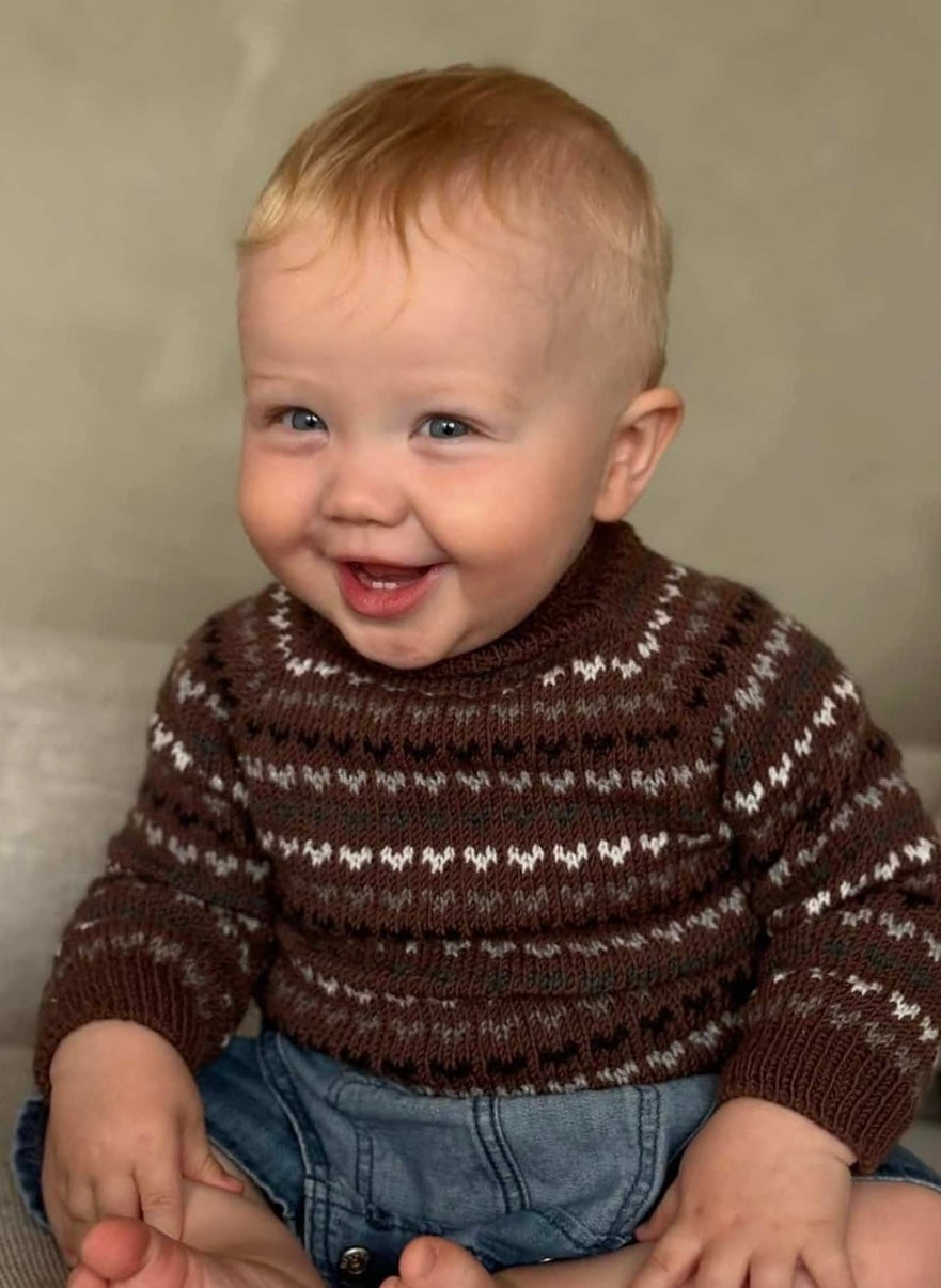 Child wearing a brown patterned sweater against a neutral background