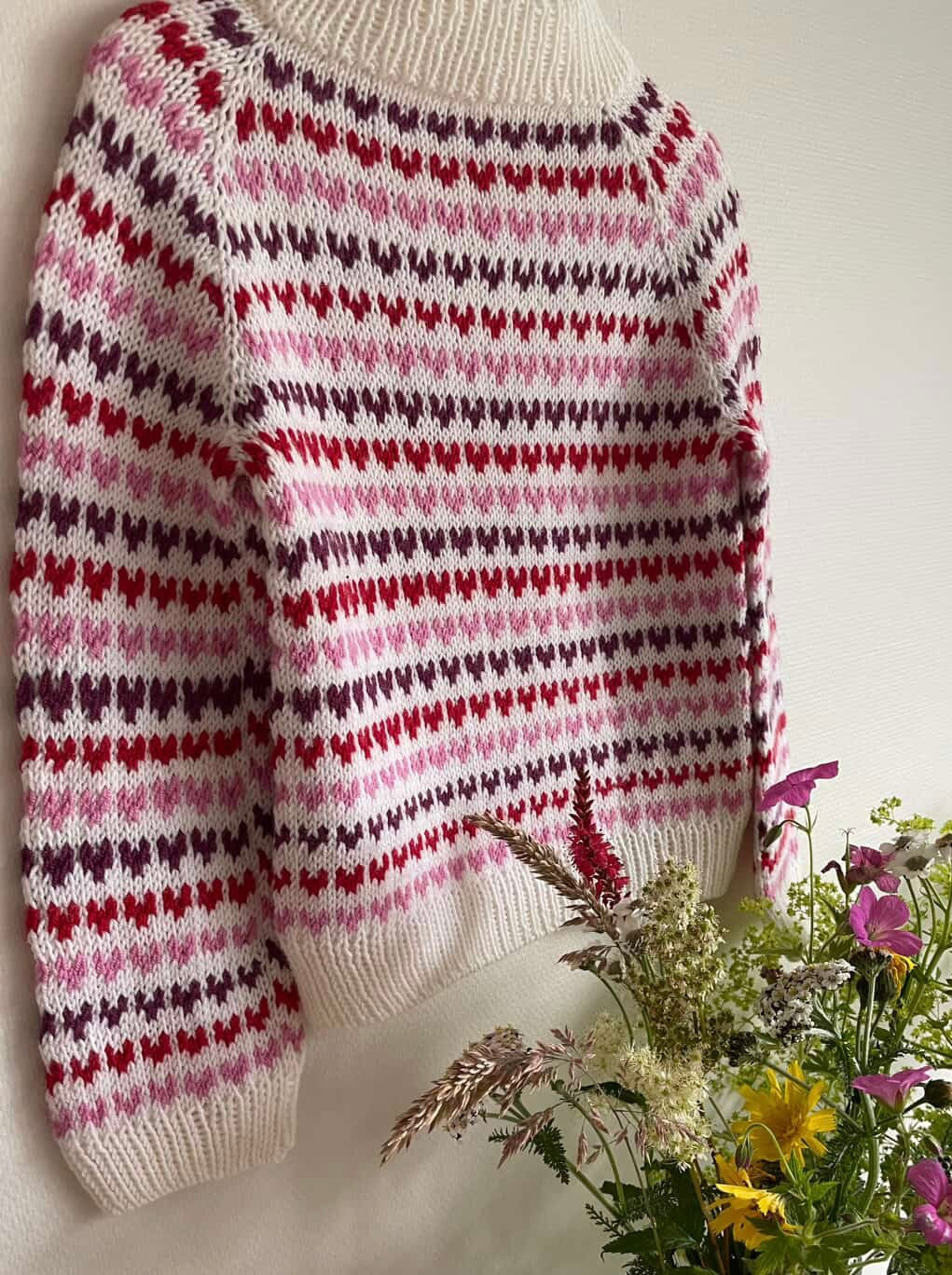 Knitted sweater with a heart pattern next to a plate of flowers on a white background