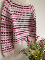 Knitted sweater with a heart pattern next to a plate of flowers on a white background
