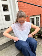 Woman sitting on steps wearing a white lace top and blue jeans, with a building in the background.