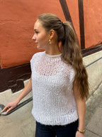Woman wearing a white knitted vest on a sidewalk.