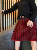Girl wearing a black top and red and black striped skirt against a striped wall.
