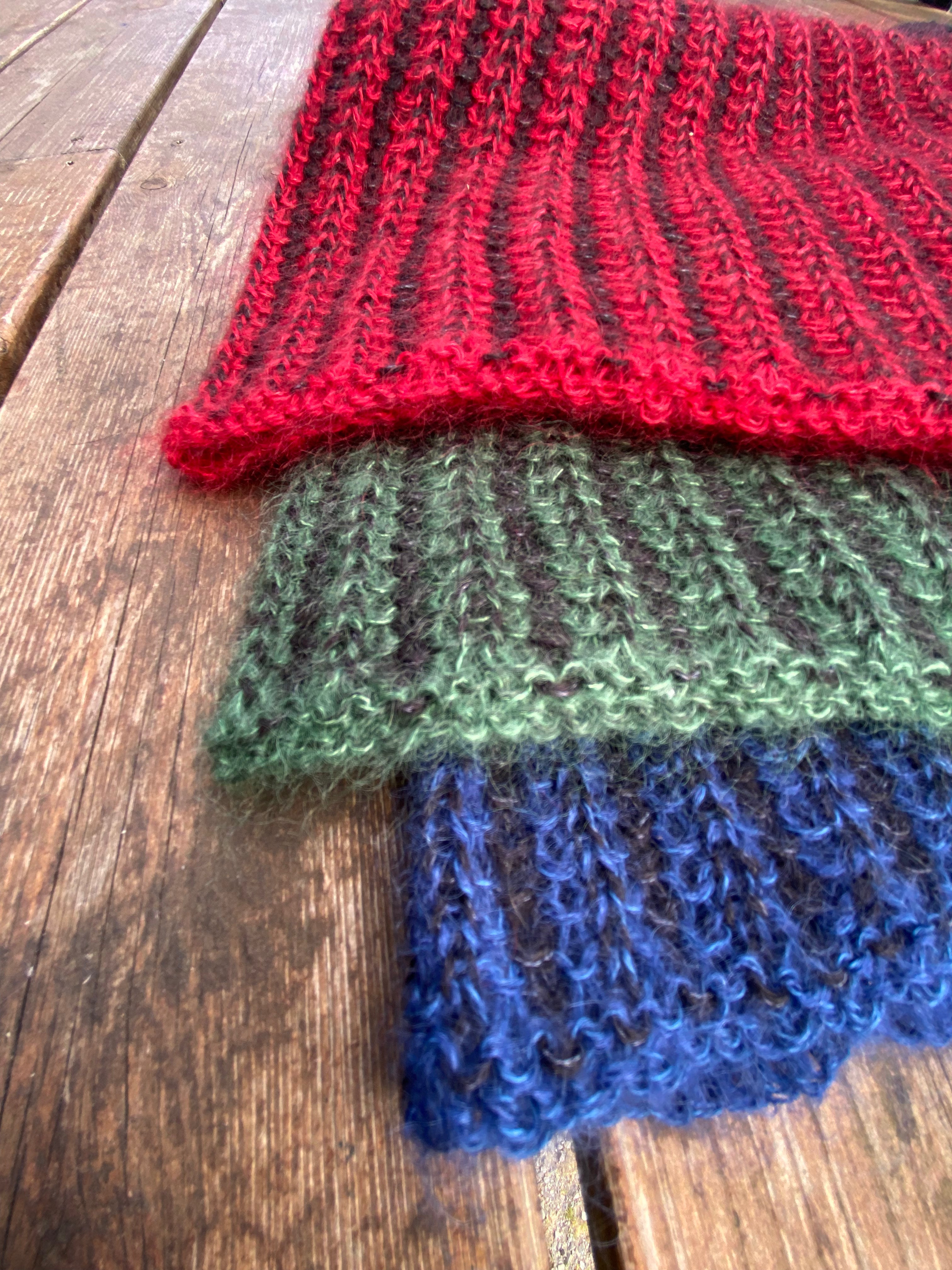 Stack of red, green, and blue knitted fabrics on a wooden surface