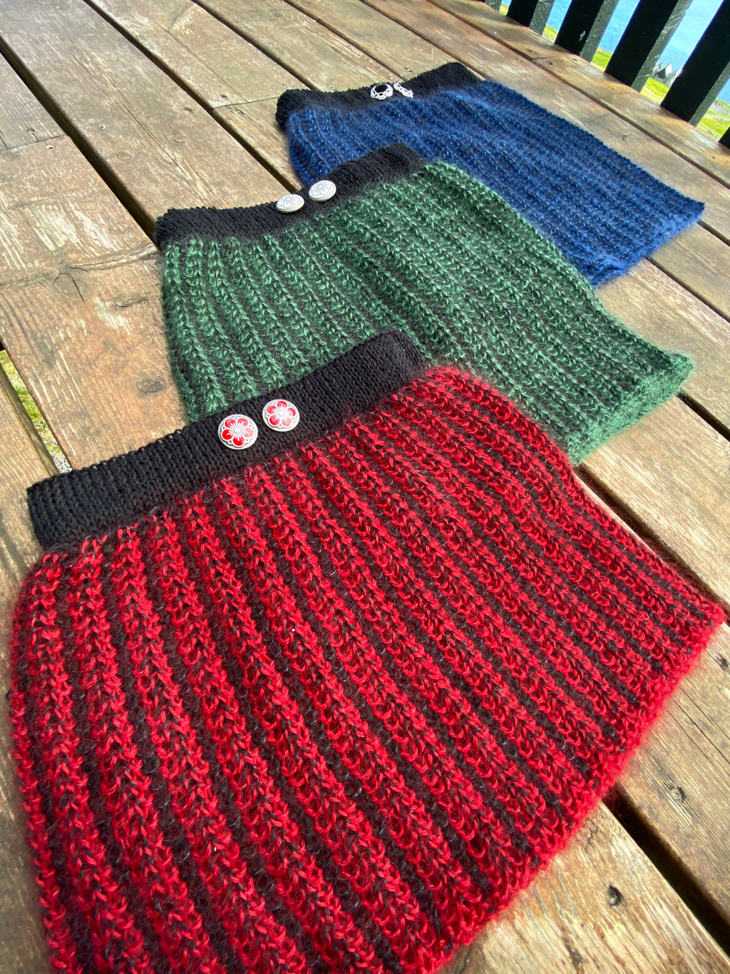Three knitted skirts in red, green, and blue on a wooden surface.
