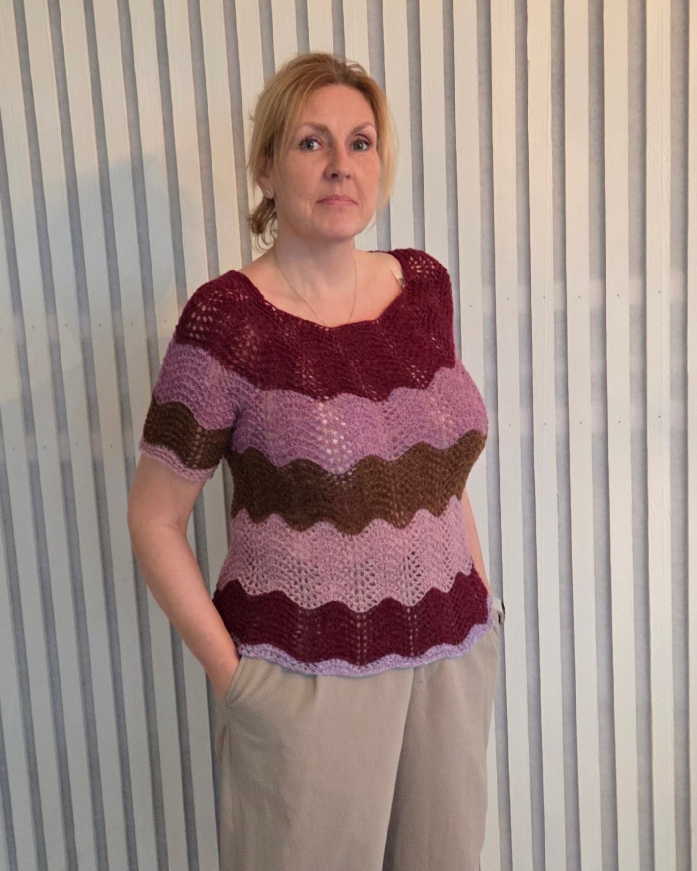 Kvinna í stuttermaðari blusu við reyðum og ljósareyðum strípum. Blusan er bundin við páfuglamynstri.