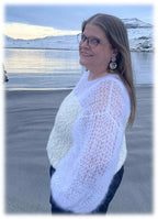 Woman wearing a white knitted blouse on a beach with a snowy landscape in the background