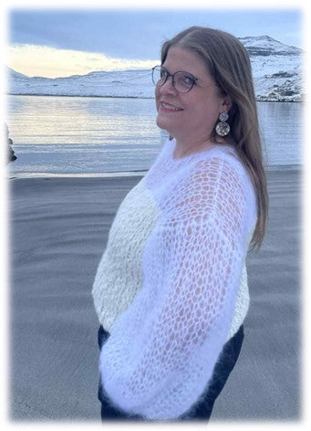 Woman wearing a white knitted blouse on a beach with a snowy landscape in the background