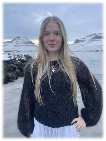 Person wearing a black knit sweater with a scenic background of mountains and water.