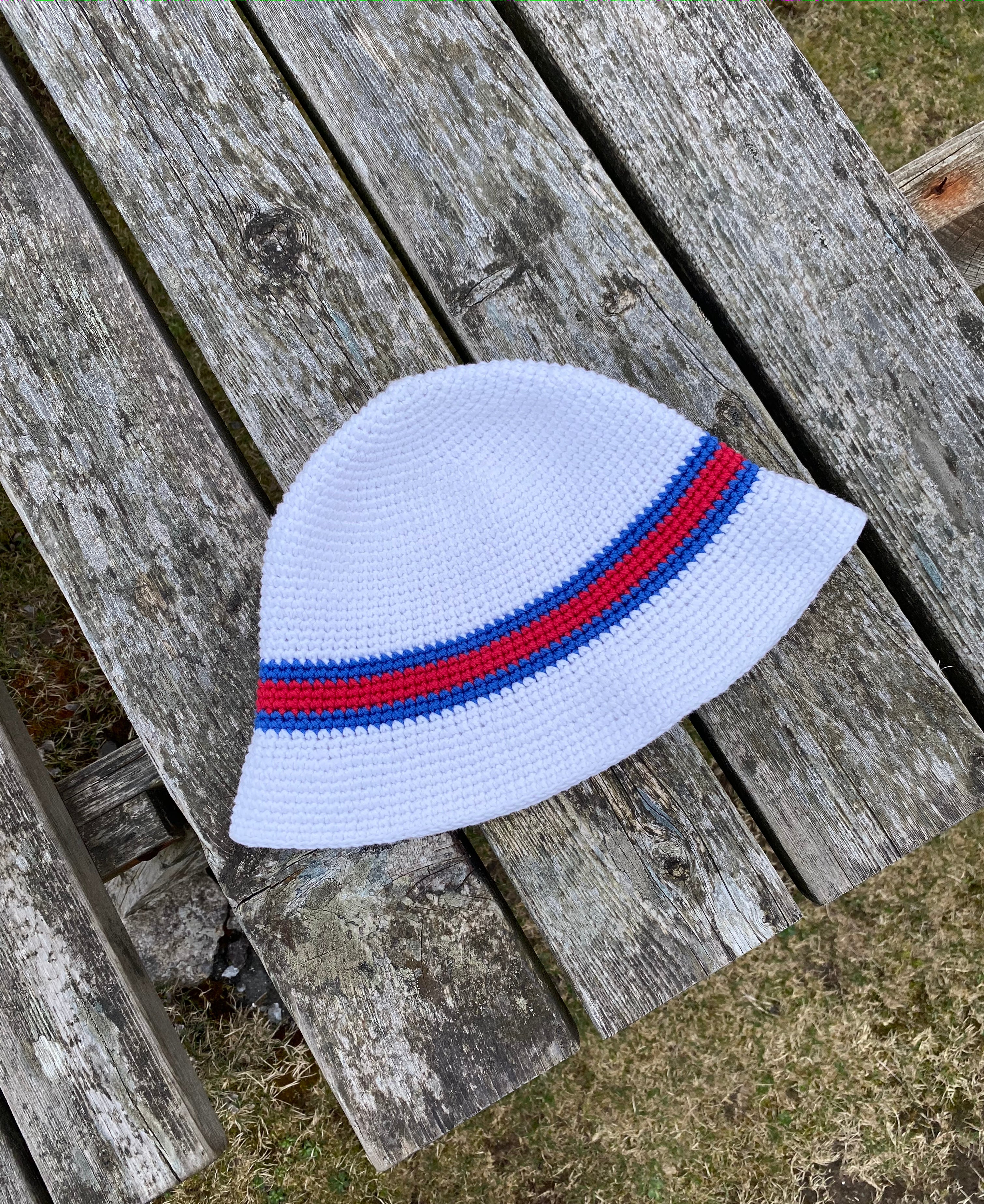 White crochet hat with red and blue stripes on a wooden surface