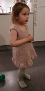 Young girl in a pink dress standing in a kitchen.