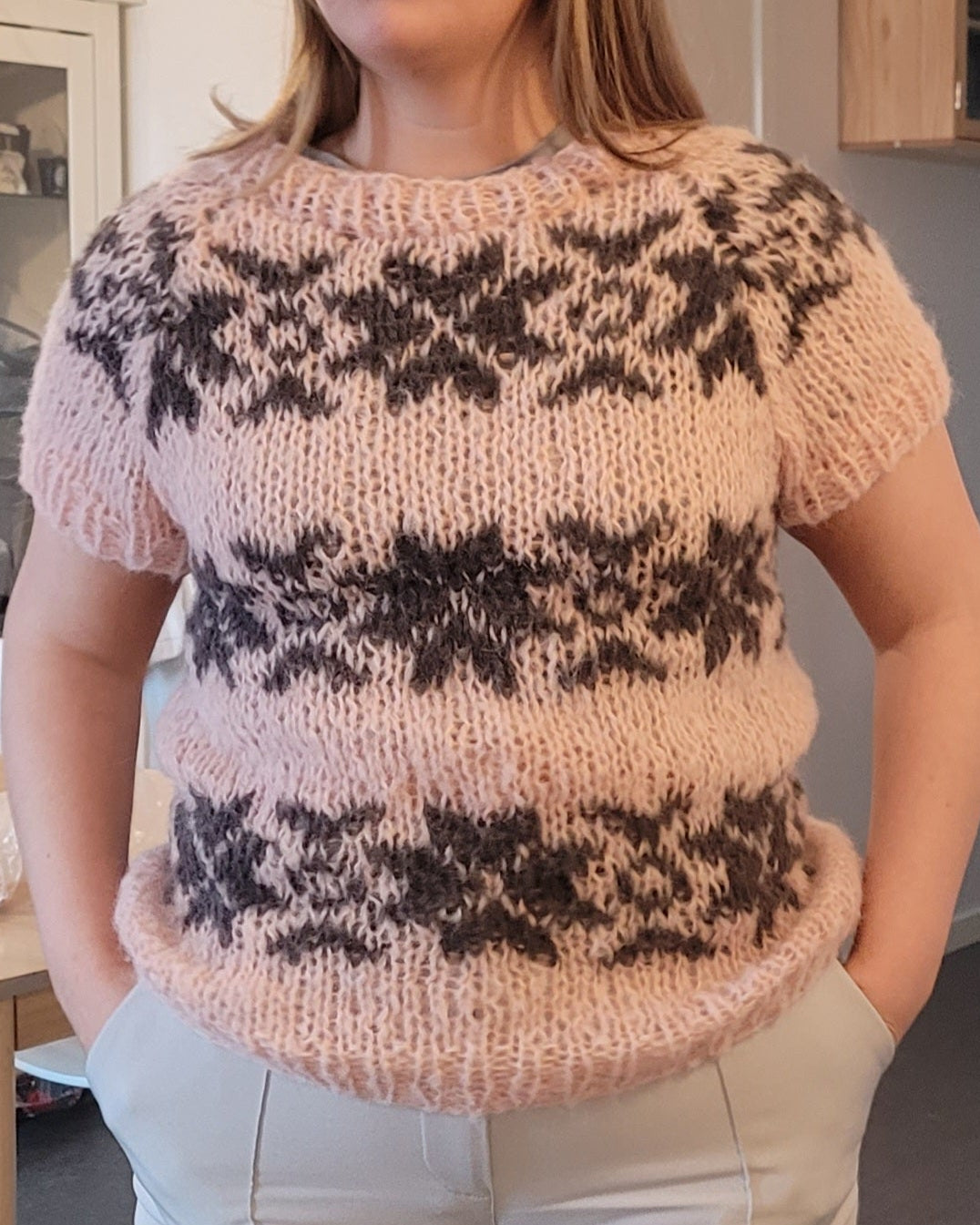 Person wearing a patterned sweater and light pants indoors.