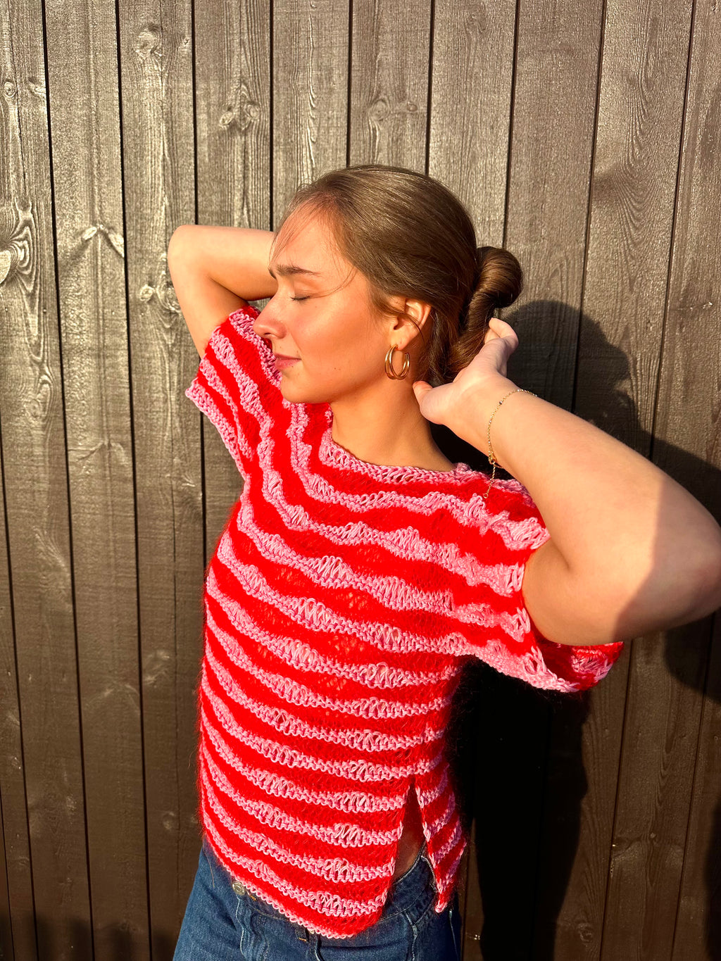 Person wearing a red and white striped shirt against a wooden fence.