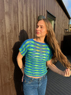 Woman wearing a blue and green striped shirt standing outdoors next to a house.