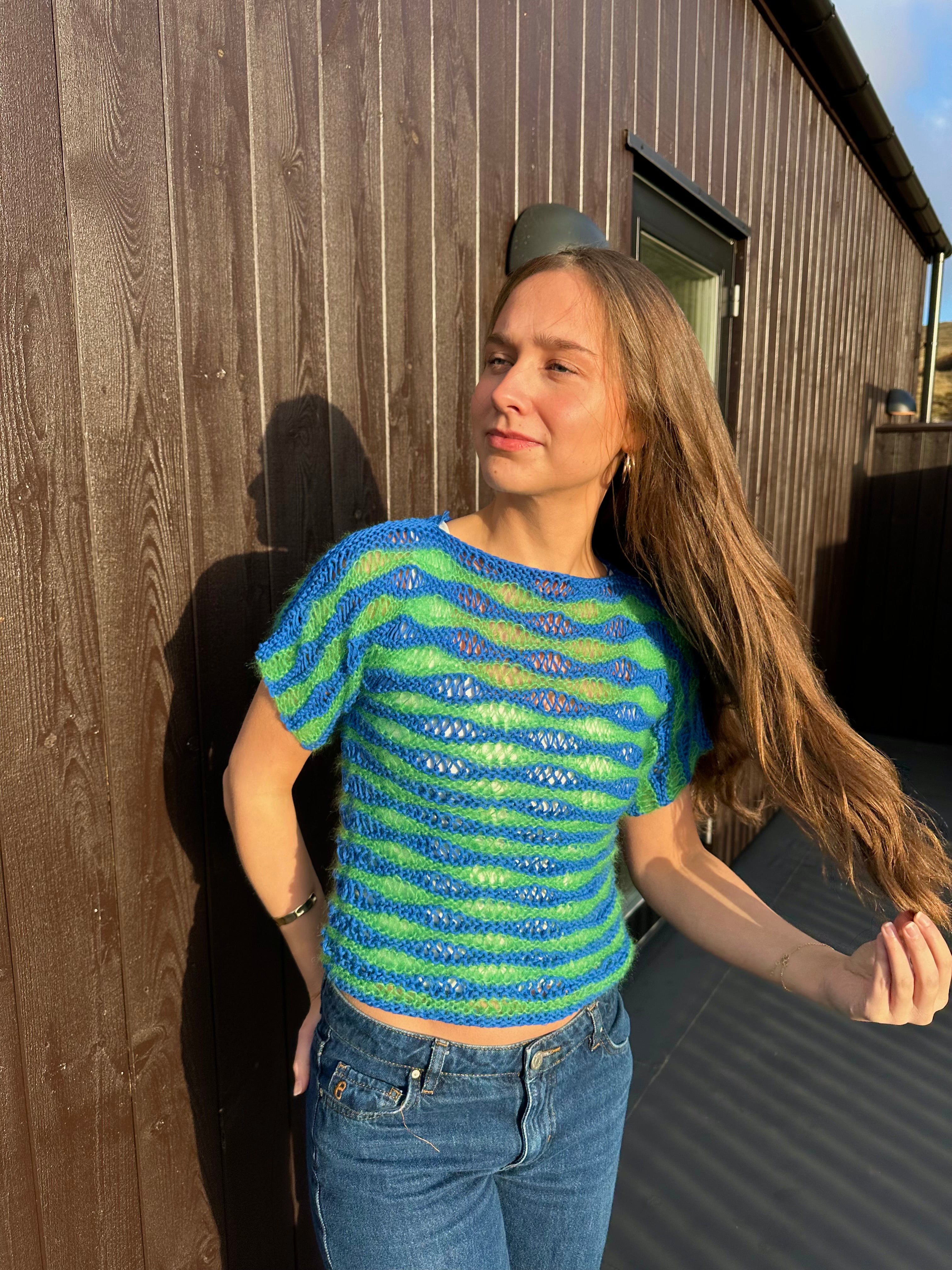 Woman wearing a blue and green striped shirt standing outdoors next to a house.