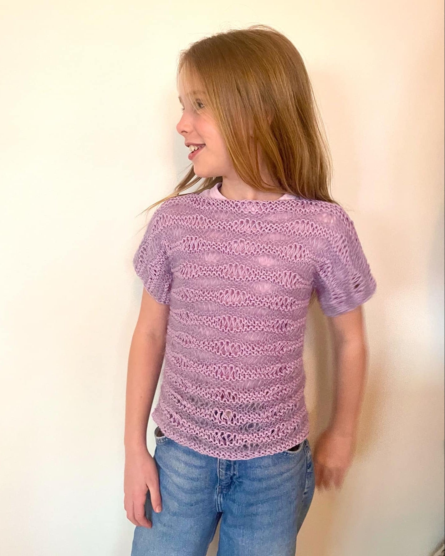 Young girl wearing a purple knitted sweater and blue jeans against a plain background