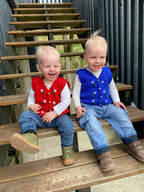 Two young boys sitting on wooden steps, wearing colorful, knitted vests.